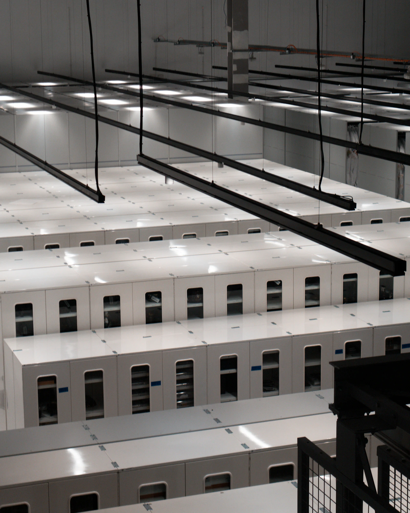 Rows of white equipment cabinets under cable trays in a data hall
