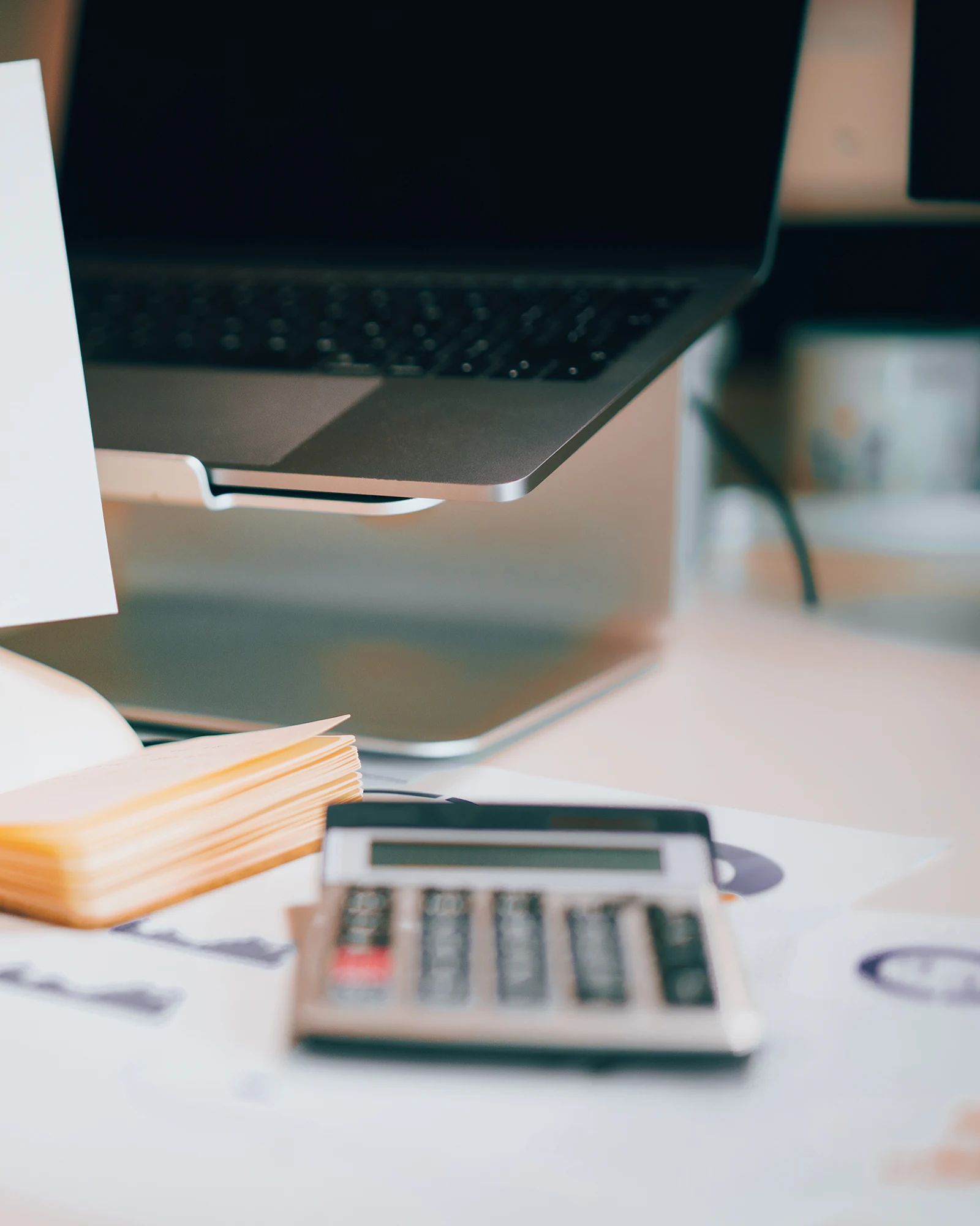 Printed charts held over a desk with a laptop, notebook, and calculator