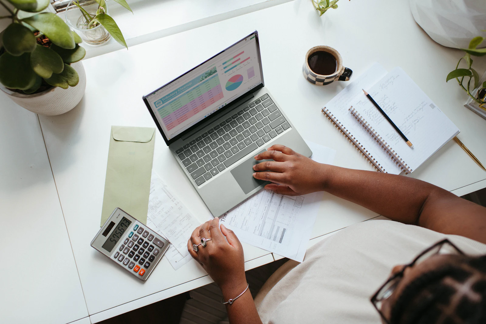 Overhead view of a spreadsheet on a laptop beside printed figures and a calculator